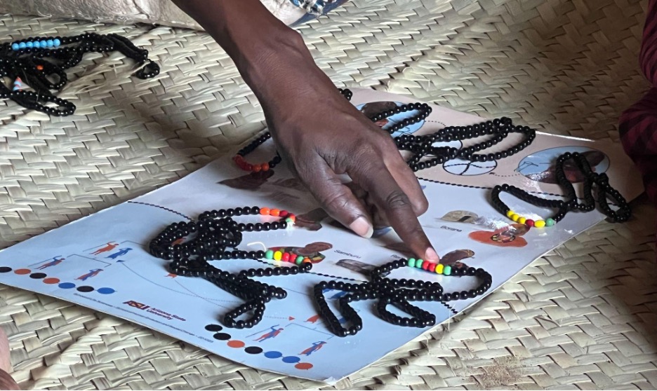Several strings of black and colored beads are scattered on top of a poster with images describing DNA. A hand points to an image on the poster.